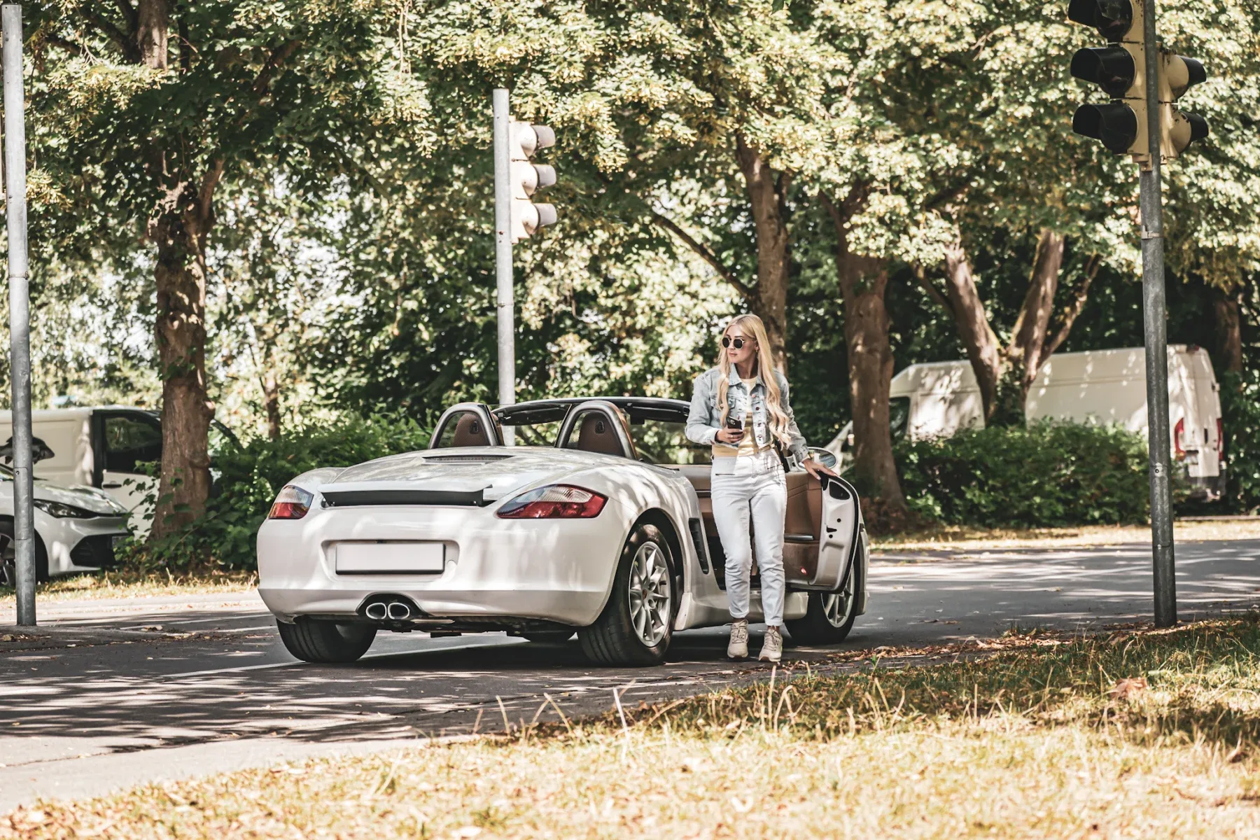 Junge Frau neben einem weißen Porsche Boxster auf einer Straße in Deutschland